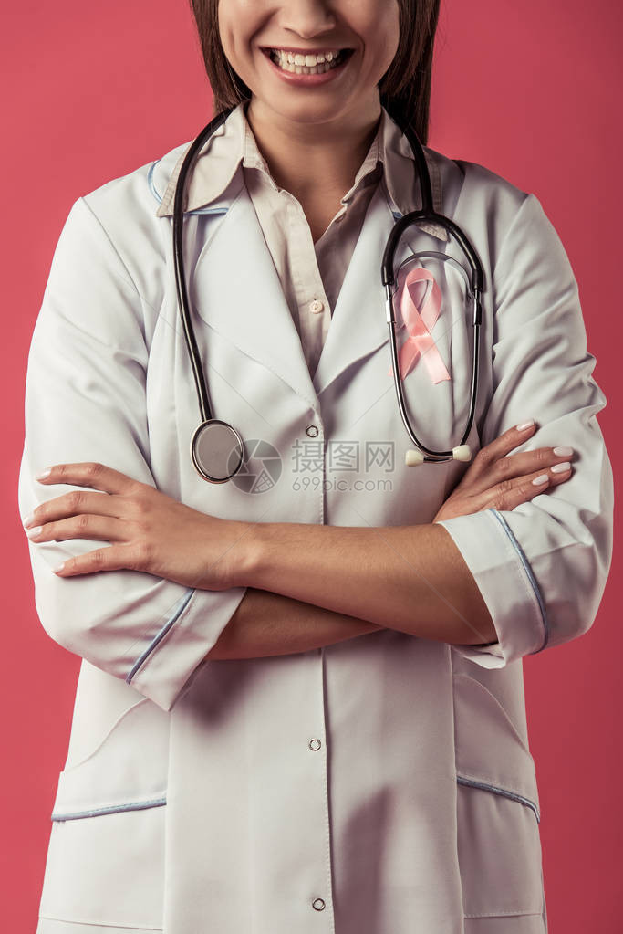 以红色背景微笑的胸前带有粉色丝带的美丽女医生被割成像图片