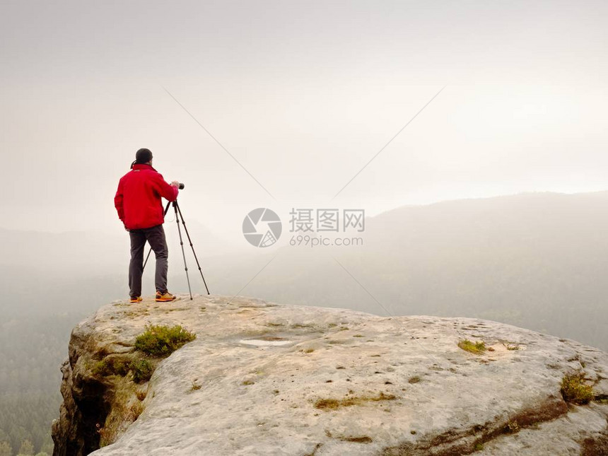 摄影师在迷雾笼罩的山峰上思考照片黎明时分在浓雾中的山谷上方拍摄雾蒙的秋天山丘和徒步旅行图片