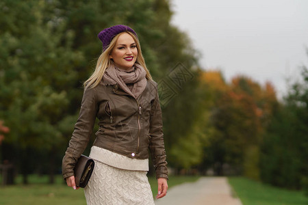 时尚的秋天穿着帽子皮夹克和手提包的时尚金发美女在秋季公园摆姿图片