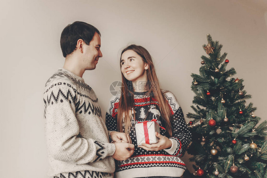 年轻夫妇在圣诞树附近用灯光交换礼物图片