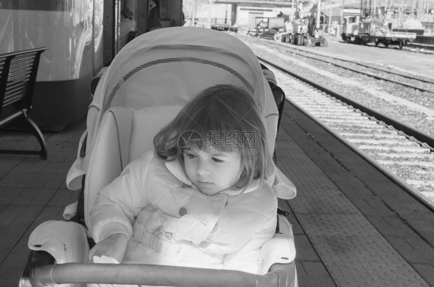 穿着温暖夹克的女婴坐在火车站的现代婴儿车里和年幼的孩子一起旅行带婴儿的家庭交通工具图片