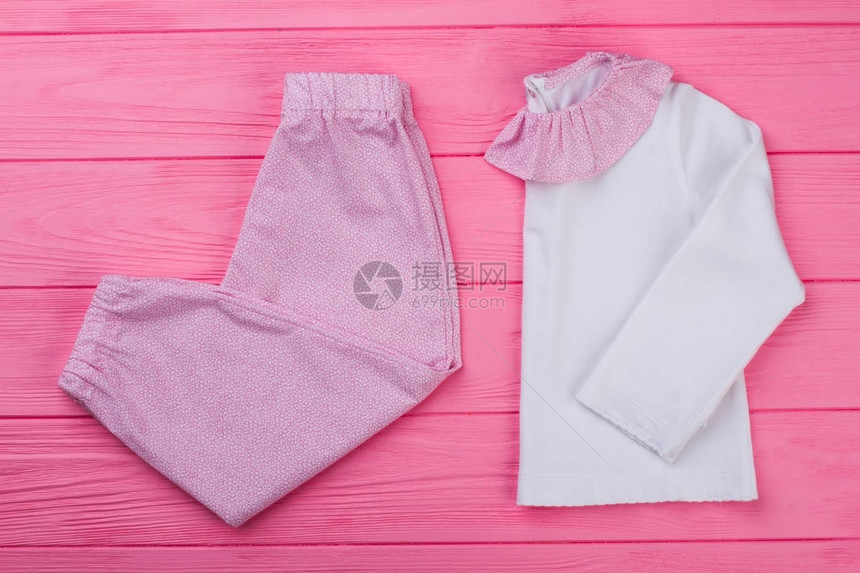 粉色和白色睡衣套在木制背景上边领和裤子的T恤适合蹒跚学步的女孩的图片