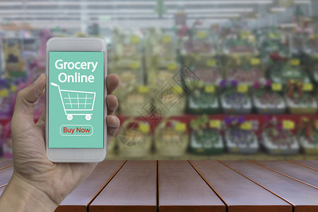 手动使用智能手机与杂货在线屏幕上模糊超市和零售店在购物图片
