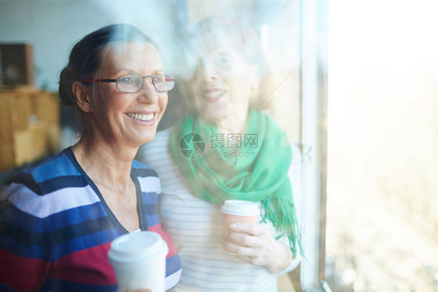 快乐的高级伙伴在阳光明媚的日子里靠窗喝咖啡图片