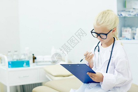 身着眼镜和白衣的小女孩在扮演医生时阅读医疗文件图片