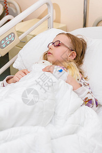 小女孩正和她的泰迪熊一起躺在医院的床上图片