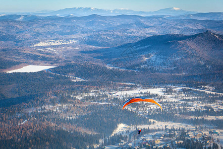一名男子带着橙色降落伞悬挂式滑翔机从滑雪胜地的雪山顶部飞行图片