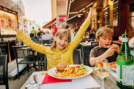 快乐的孩子们在户外餐厅吃汉堡和炸薯条和披萨图片