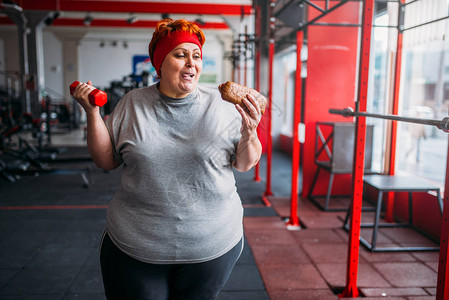 肥胖妇女与斋戒食物和哑铃在手刺激艰苦锻炼在健身房图片