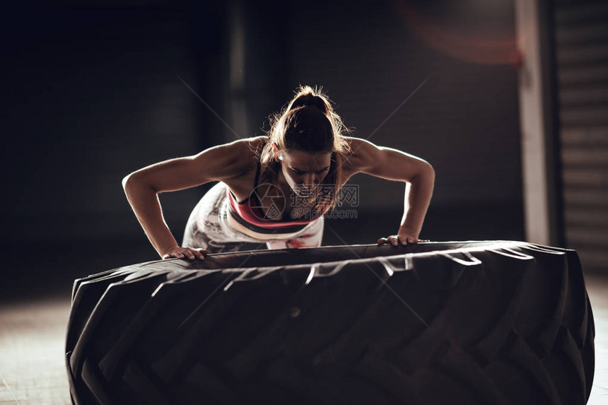 crossfit训练的年轻肌肉妇女在轮胎上做俯卧撑锻炼图片