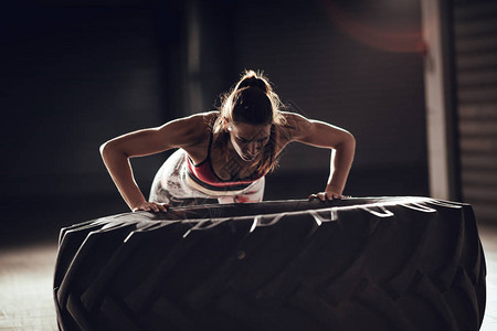 crossfit训练的年轻肌肉妇女在轮胎上做俯卧撑锻炼图片