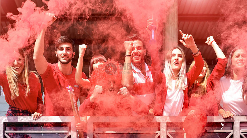 年轻的球迷欢呼与彩色烟雾观看足球比赛一起在体育场朋友的人组与红色t恤有兴奋的乐趣体育世界锦标赛概念图片