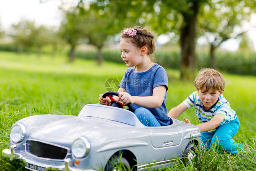 两个快乐的孩子们玩在夏天的花园里室外大旧玩具车图片