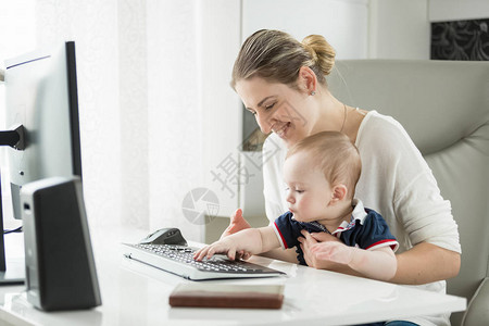年轻母亲的肖像教她的孩子使用计算机和键盘打字图片
