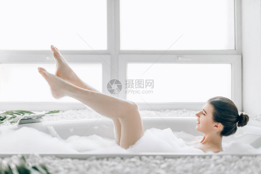 有魅力的妇女躺在浴缸与泡沫和显示腿放松健康和护肤概念图片