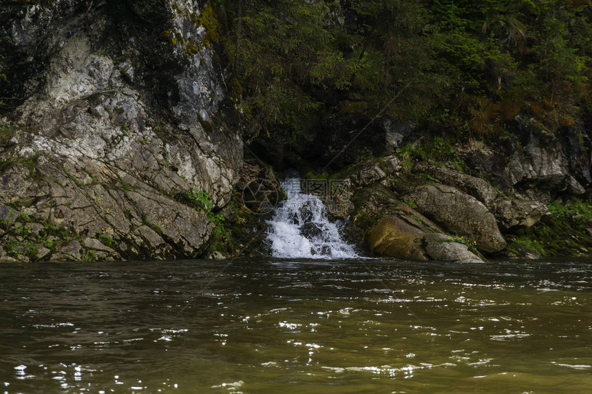 泉水沿着岩石的瀑布流进河中在一条图片