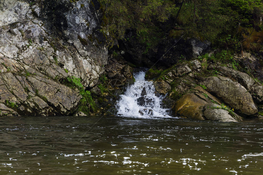泉水沿着岩石的瀑布流进河中在一条图片
