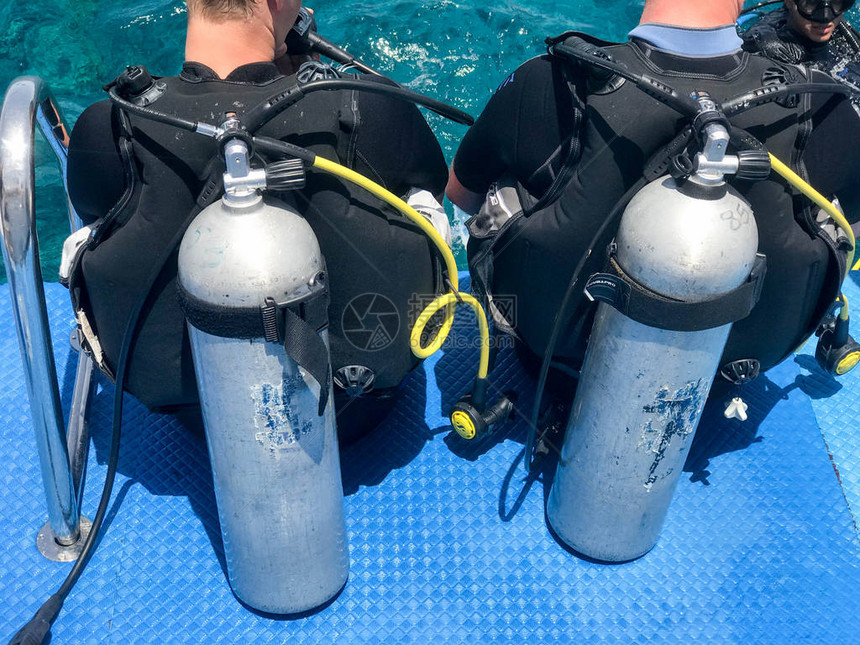 两名男潜水员在黑色潜水防水西装与闪亮的金属铝罐准备从船上潜水到蓝色的海水图片