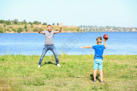 愉快的父亲和儿子在河附近演奏橄榄球图片
