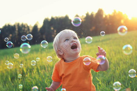 可爱的金发男孩玩肥皂泡在夏天的领域快乐的童年概念真实的生活方式形象图片