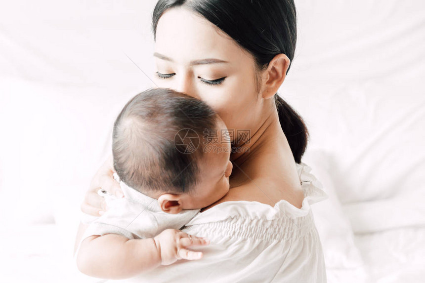 母亲抱着婴儿在她的怀里亲吻在一个白色的卧室对家庭概念的爱图片