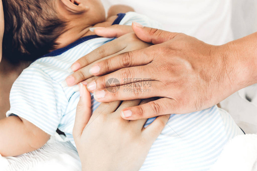 母亲和父亲抱着婴儿在她的怀里在一个白色的卧室对家庭概念的爱图片