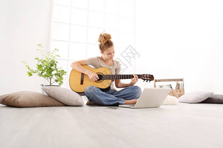 美丽的年轻女吉他与电脑玩在线课程坐在地板上的休闲服装在家中图片