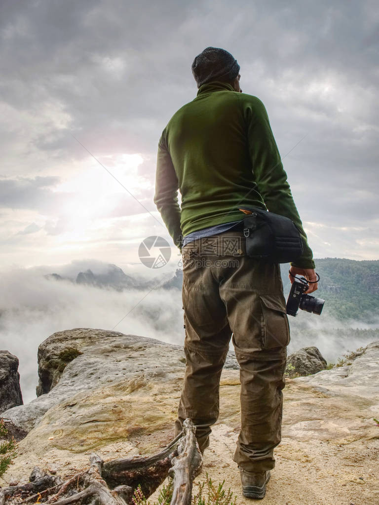 在山崖上看雾的摄影师徒步旅行者将拍照与小照相机在手图片