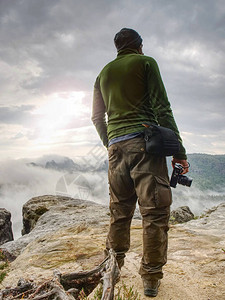 在山崖上看雾的摄影师徒步旅行者将拍照与小照相机在手图片