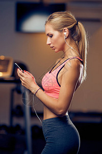 妇女在健身房里使用智能手机在后台跑步机健康的生活方式概念图片