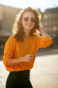 积极的年轻女子戴着镜穿着时髦的衣服走在阳光明媚的街道图片