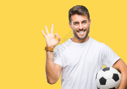 年轻的帅哥把足球球抱在孤立的背景上做好手指标志优秀的标志背景图片