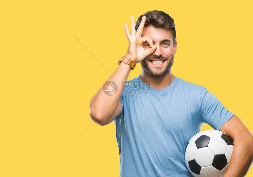 年轻的帅哥把足球球抱在孤立的背景上脸上洋溢着幸福的笑容做着确定的标志用手盯着手指图片