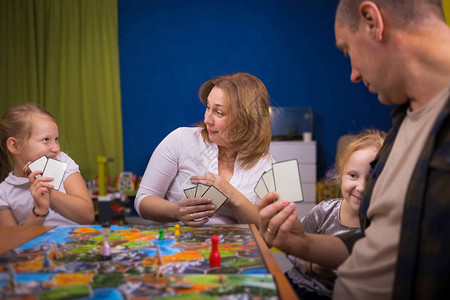 棋盘游戏概念一家人正在家里玩棋盘游戏棋盘游戏场许多数字硬币和沙漏四个人在脸上玩持卡片的快乐情绪背景图片