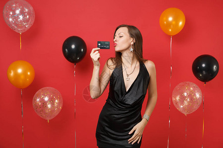 80周年校庆感的年轻女人穿着小黑裙庆祝拿着信用卡吹着嘴唇在鲜红的背景气球上送空气吻新年快乐生日模拟节日聚会理念背景