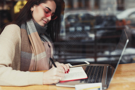 漂亮的黑发女人在咖啡馆工作戴着眼镜在窗户附近的笔记本电脑里聊天图像背景图片