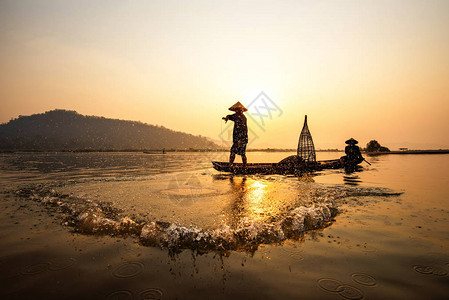 亚洲渔夫网在木船上撒网日落或苏打背景图片
