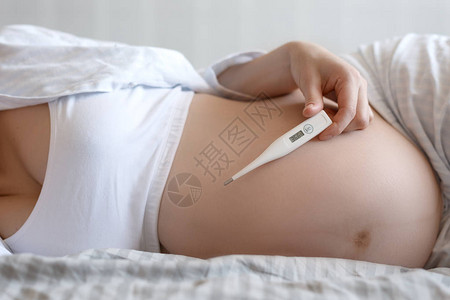 手握电子体温计的孕妇腹部特写孕期妇女健康的概念图片