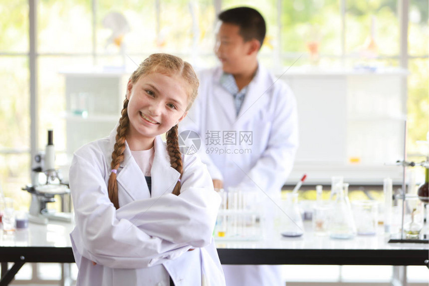 自信好奇的小女孩站在科学实验室里笑容满面另一个孩子背景模糊教育与科学家概念图片