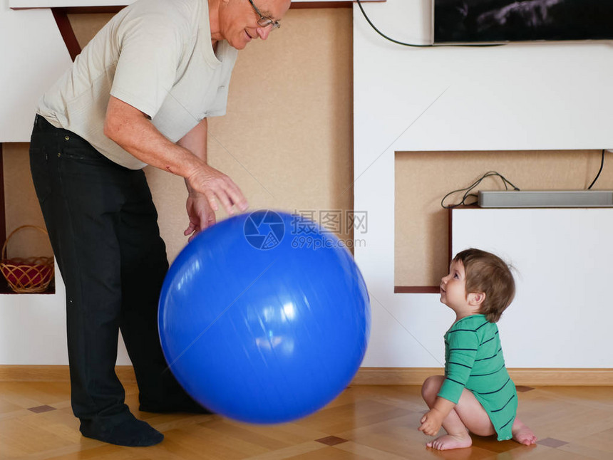 这孩子和爷爷玩球在家里打一个大球一个男孩正在和他的祖父玩图片
