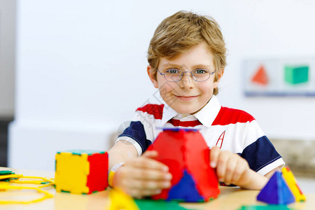 戴着眼镜的小男孩在学校或学前托儿所玩lolorful塑料元素套件快乐的孩子建造和创造几何图形背景图片