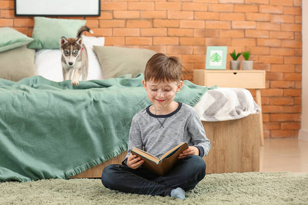 小男孩和可爱的哈士奇小狗在卧室看书图片