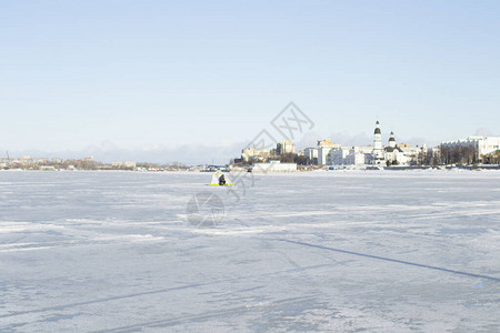 在城市背景的冰上渔夫靠近风边的帐篷图片