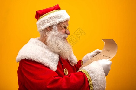 快乐的圣诞老人拿着黄色背景的老式纸圣诞快乐和前夜的概念复制空间阅读困难背景图片