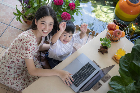 亚洲母亲在家里的花园里用笔记本电脑教儿子图片