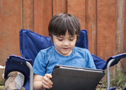 活跃的孩子坐在花园的椅子上玩游戏或在平板电脑上看卡通片图片