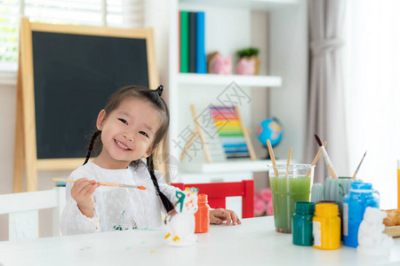 亚洲幼儿园女学生在家里的客厅里用丙烯酸水彩颜料画石膏娃图片