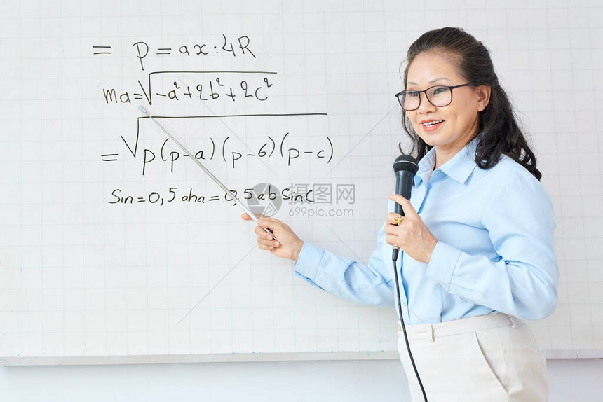 数学老师在指着白板上的方程式和向学生解释新课题时用麦克风说图片