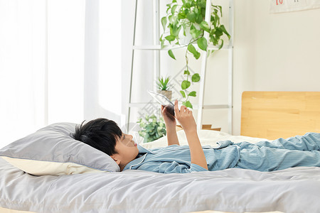 小男孩在床上玩手机背景图片