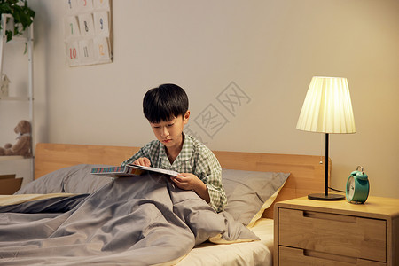 看书晚上小男孩坐在床上看书背景